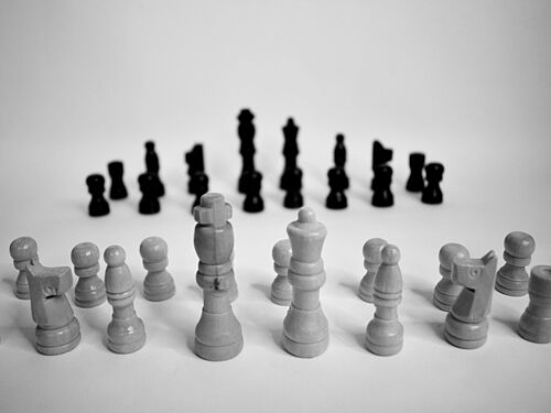 Schwarze und weiße Schachfiguren sind in gegenüberliegenden Reihen auf einer glatten Oberfläche angeordnet und schaffen ein Gefühl von Vorfreude und Strategie in einem minimalistischen Umfeld.