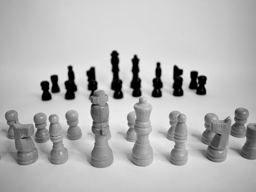 Schwarze und weiße Schachfiguren sind in gegenüberliegenden Reihen auf einer glatten Oberfläche angeordnet und schaffen ein Gefühl von Vorfreude und Strategie in einem minimalistischen Umfeld.